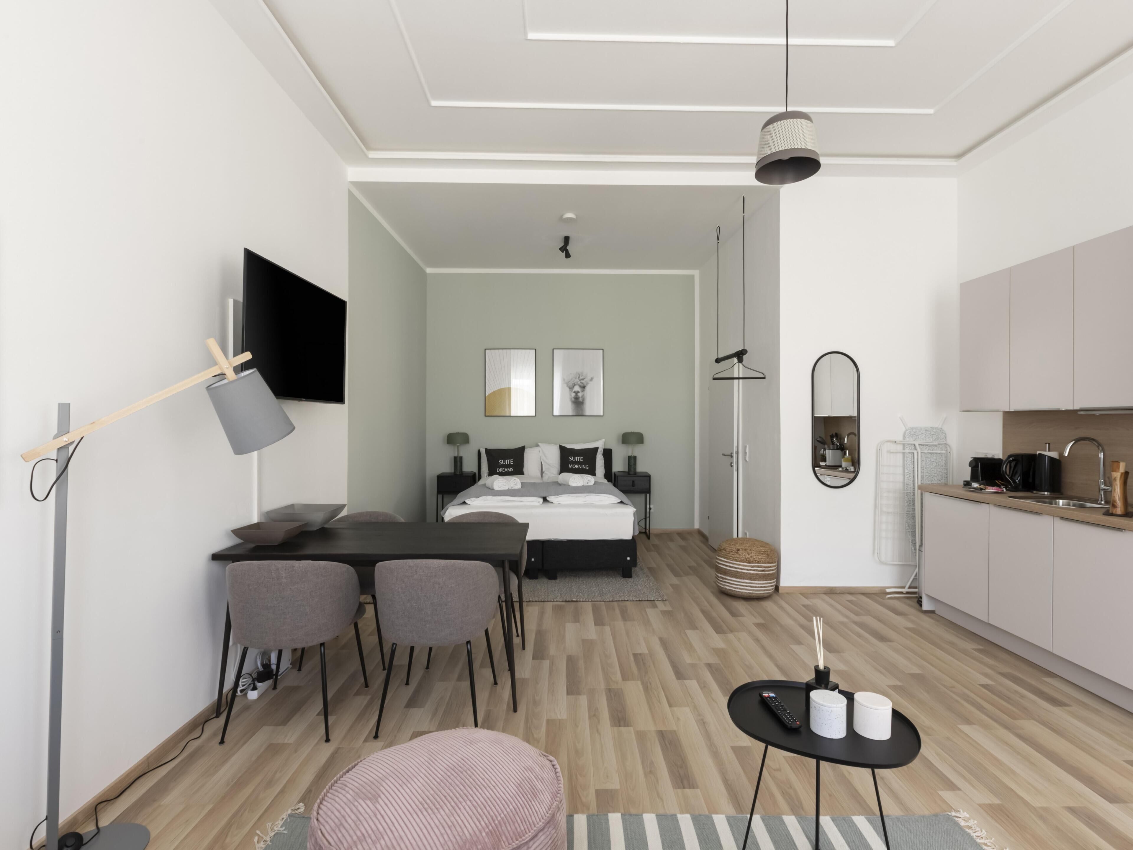 A modern hotel room with a bed, bedside table, and a view of the kitchen.
