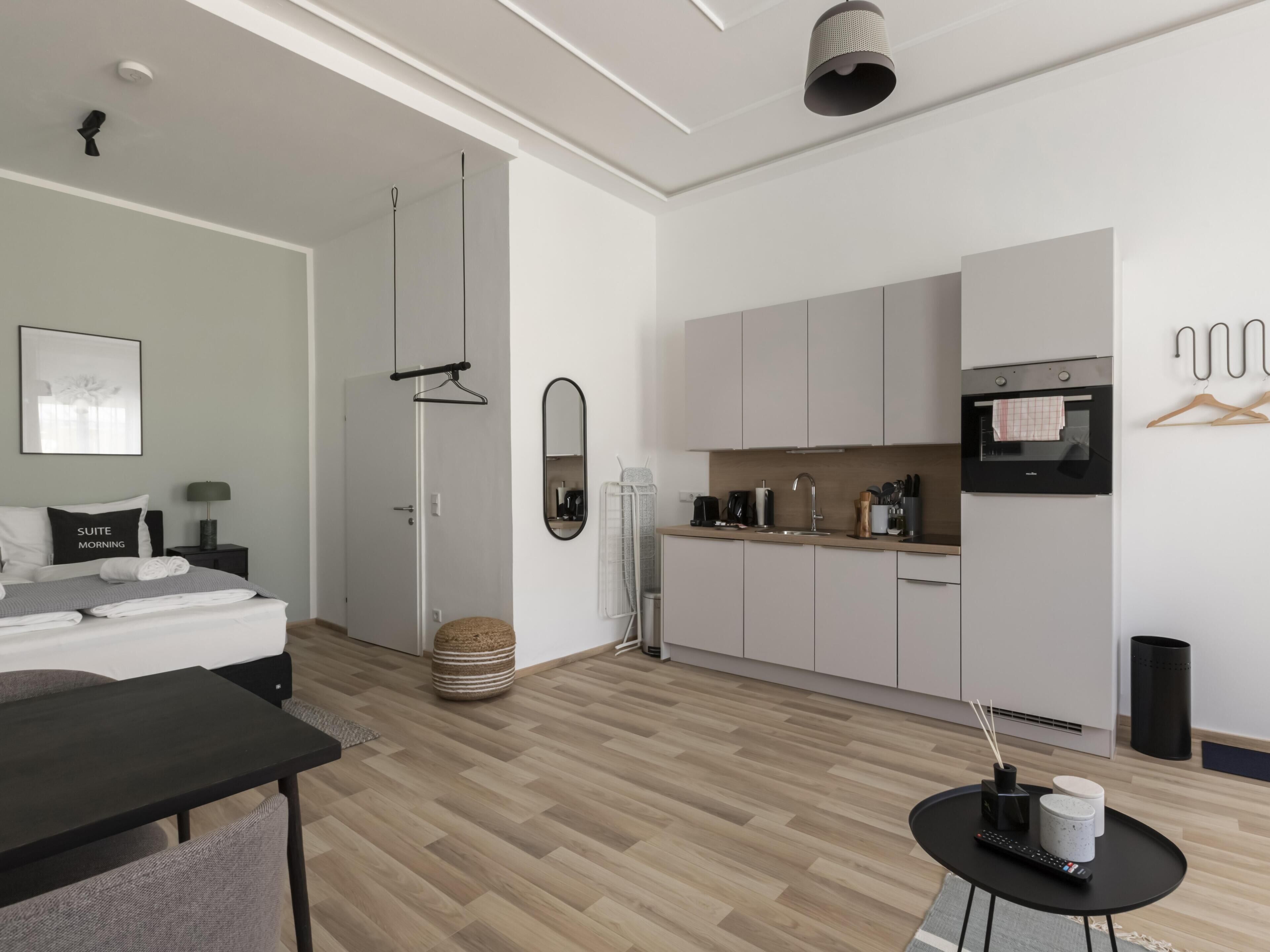 A modern, minimalist hotel room with a bed, bedside table, and a small dining area.