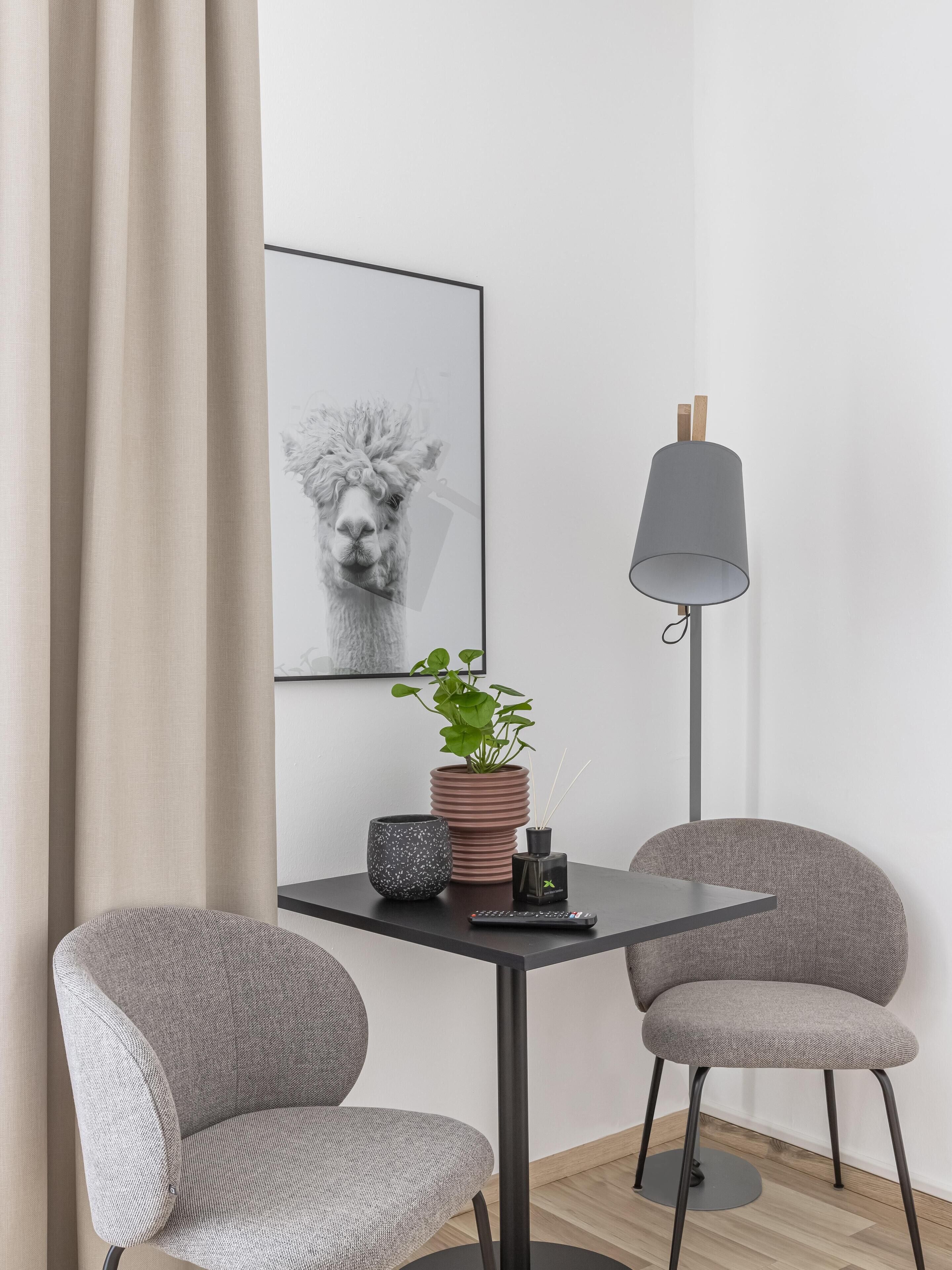 A modern room with a table, two chairs, a floor lamp, a potted plant, a framed picture, and a remote control.