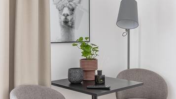 A modern room with a table, two chairs, a floor lamp, a potted plant, a framed picture, and a remote control.