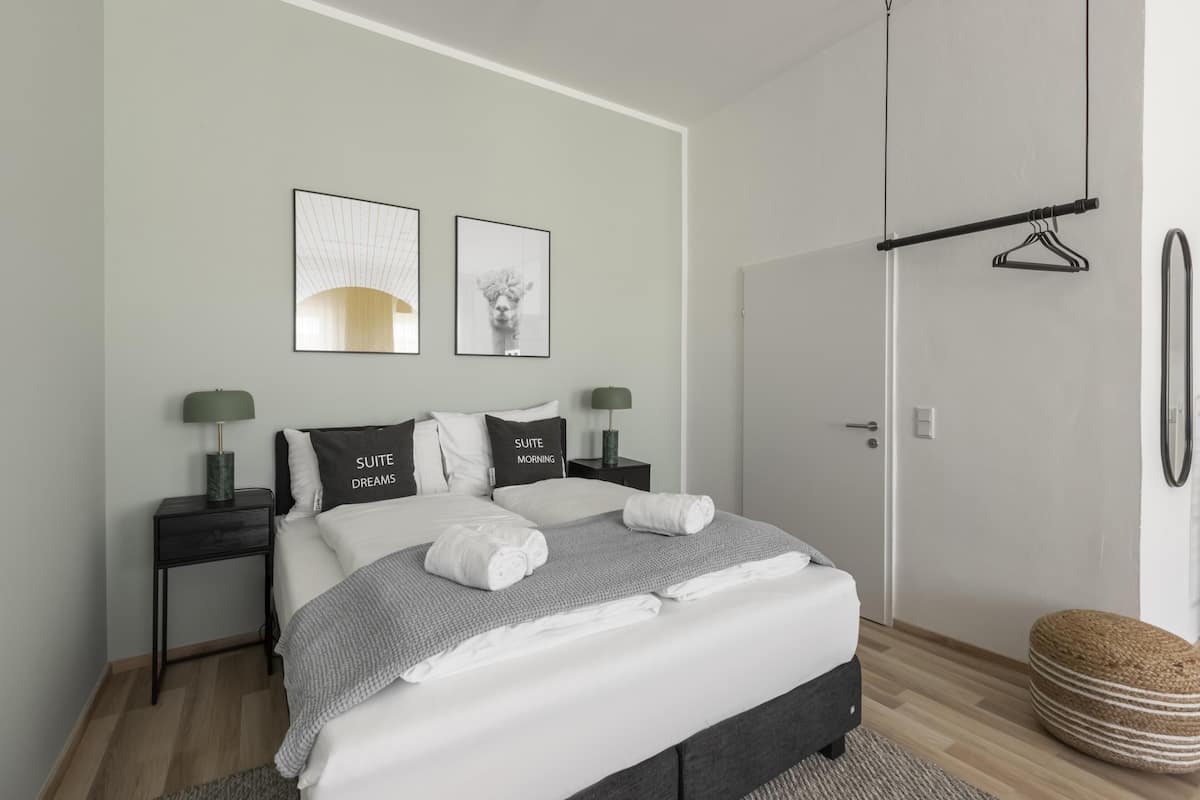 A modern bedroom with a bed, two bedside tables, a hanging light, and a door.