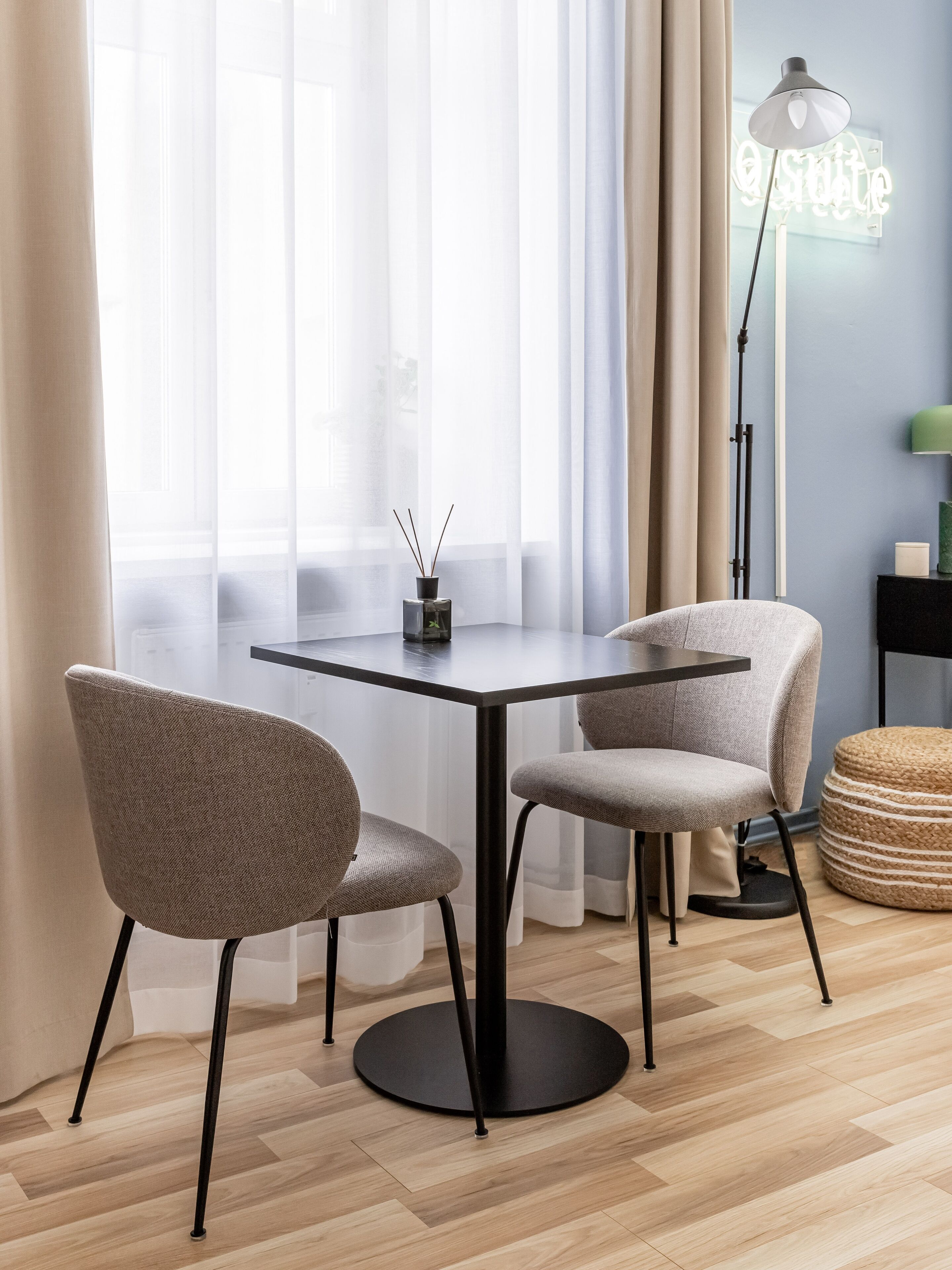 A modern dining area with a table and chairs, a floor lamp, and a neon sign.