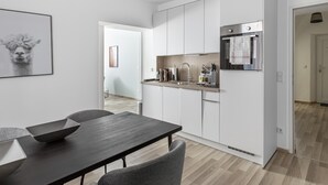Una cocina moderna con armarios blancos, un refrigerador de acero inoxidable y un horno empotrado. Hay una zona de comedor con una mesa y sillas oscuras.