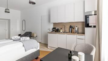 A modern, minimalist hotel room with a bed, bedside table, and a small kitchenette.