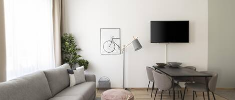 Un soggiorno moderno con un divano grigio, un tavolo da pranzo con sedie, un televisore nero e un quadro raffigurante una bicicletta appesa al muro.