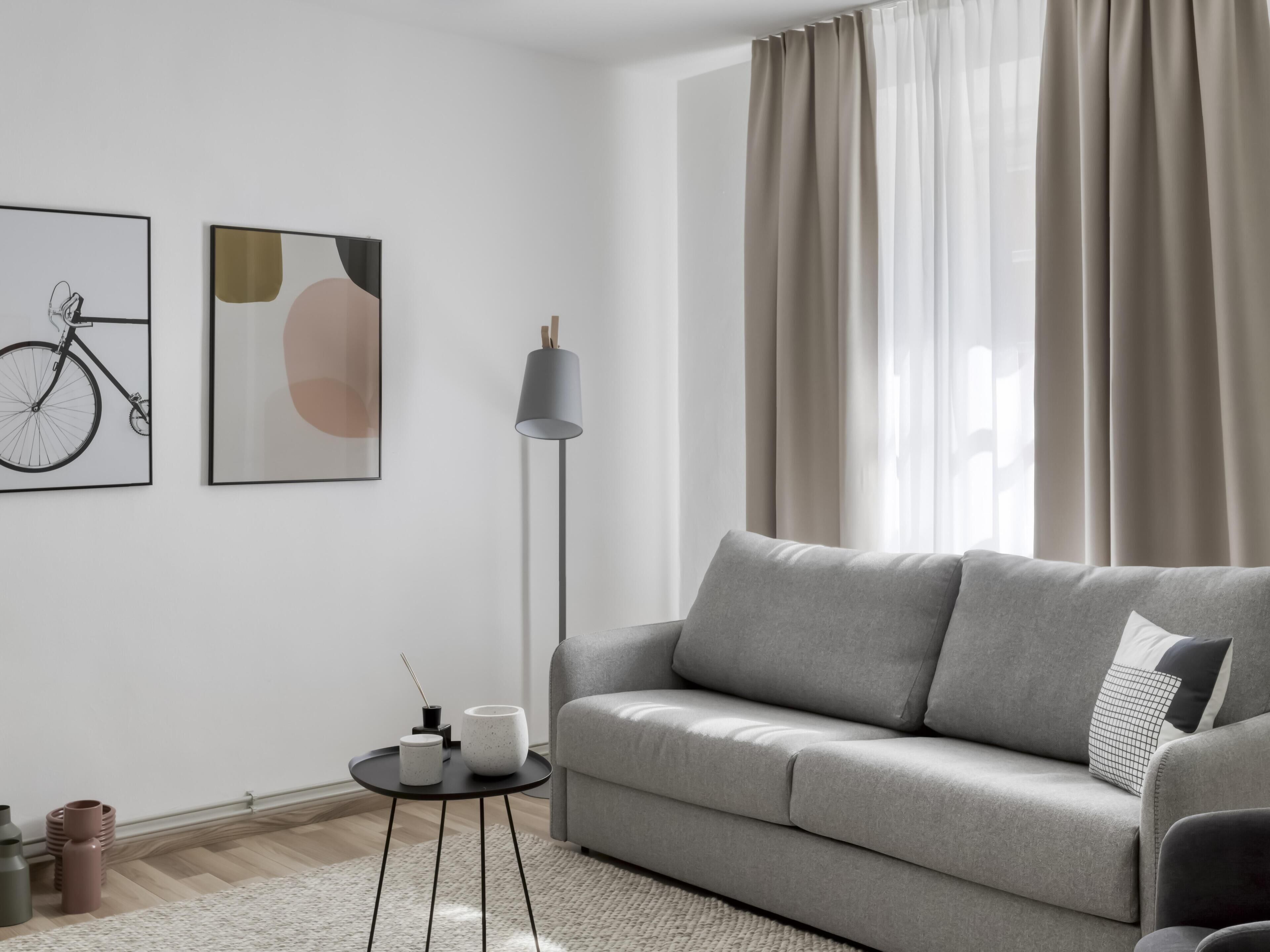 A modern living room with a grey sofa, a floor lamp, and two wall-mounted abstract paintings.