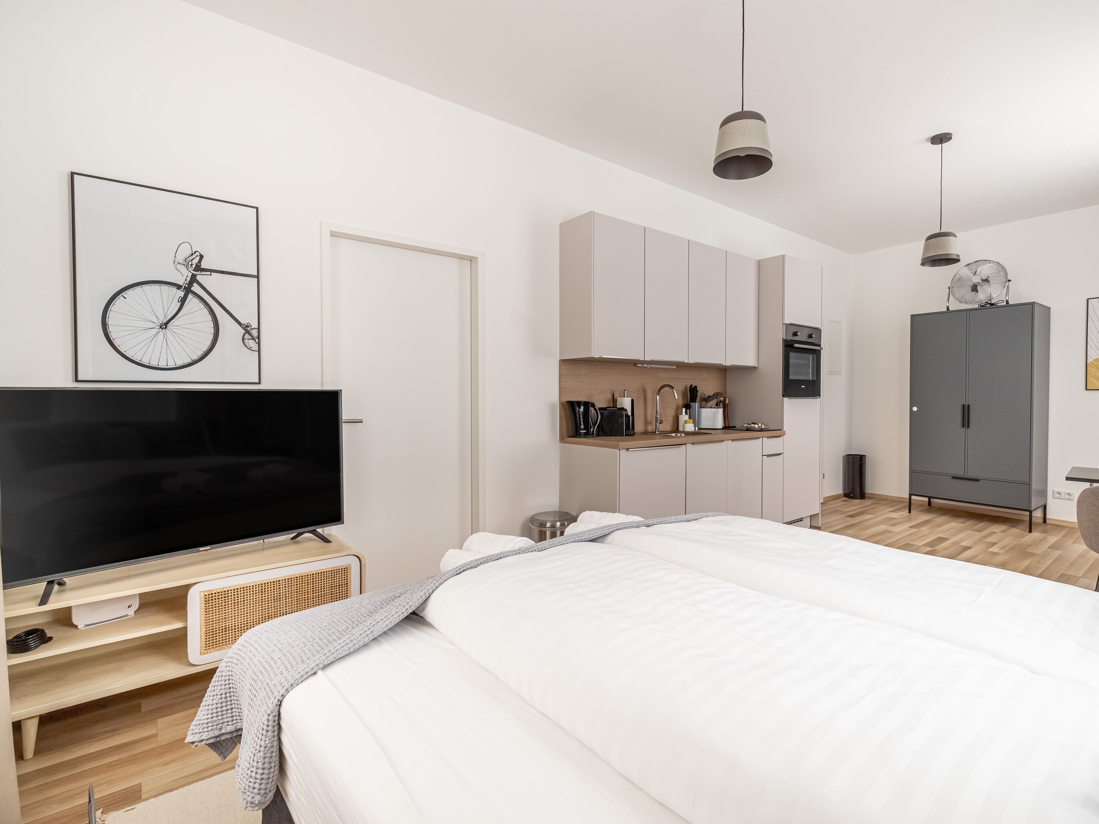 A modern bedroom with a large bed, a TV, a kitchenette, and a wardrobe.