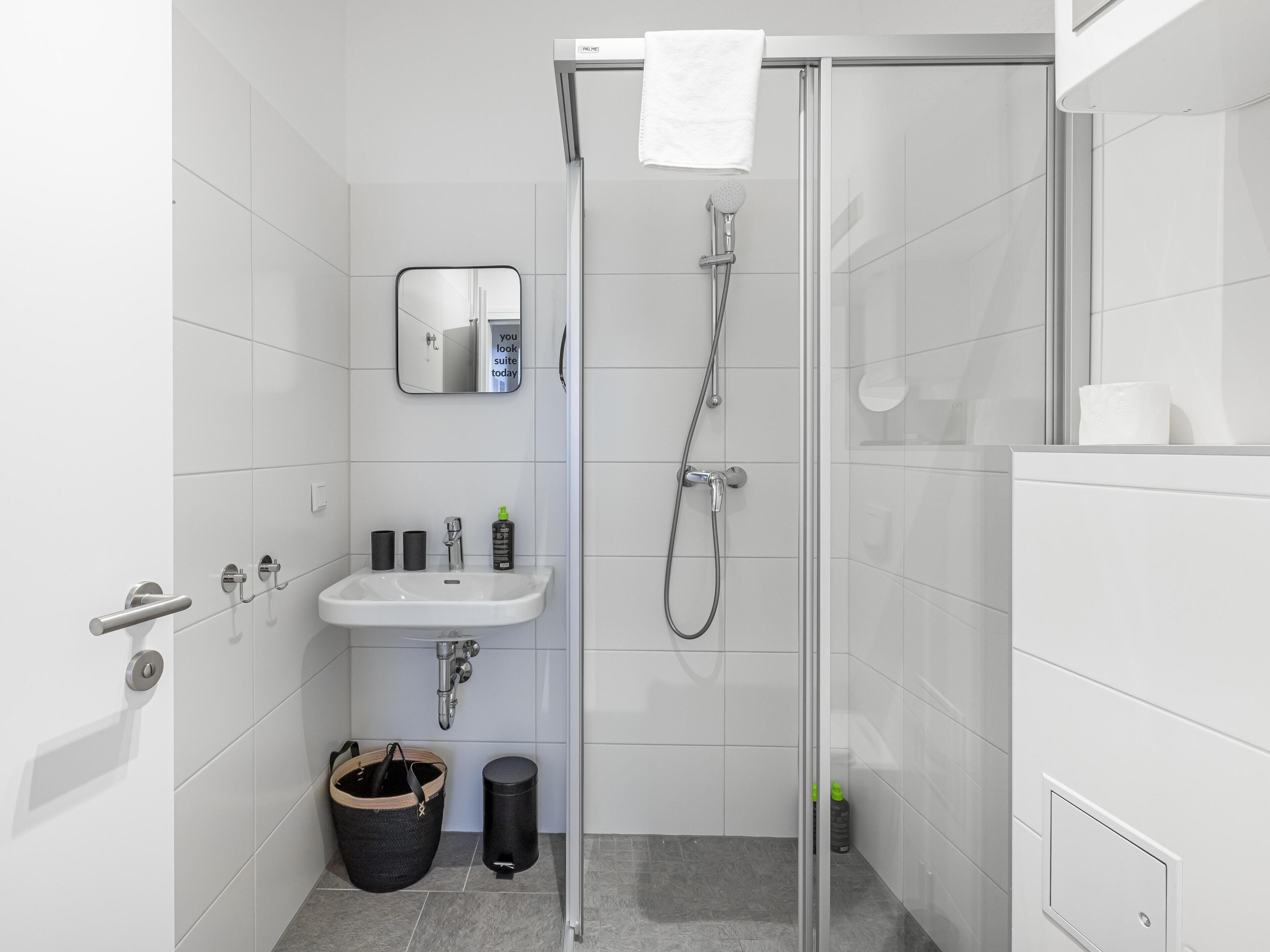 Ein modernes Badezimmer mit Duschkabine aus Glas, Waschbecken, Spiegel und Handtuchhalter.
