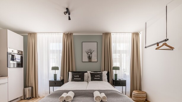 Una habitación de hotel moderna con una cama grande, dos mesitas de noche, una lámpara colgante y vistas de la ciudad a través de amplios ventanales.