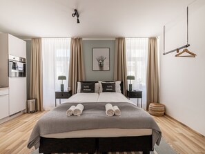 A modern hotel room with a large bed, two bedside tables, a hanging light fixture, and a view of the city through large windows. - Limehome Villach Kirchenplatz (Villach)