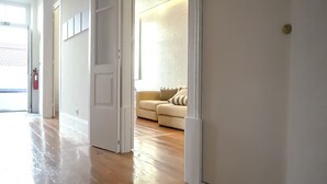 Un couloir au plancher de bois menant à un salon avec un canapé beige et un mur en briques blanches.