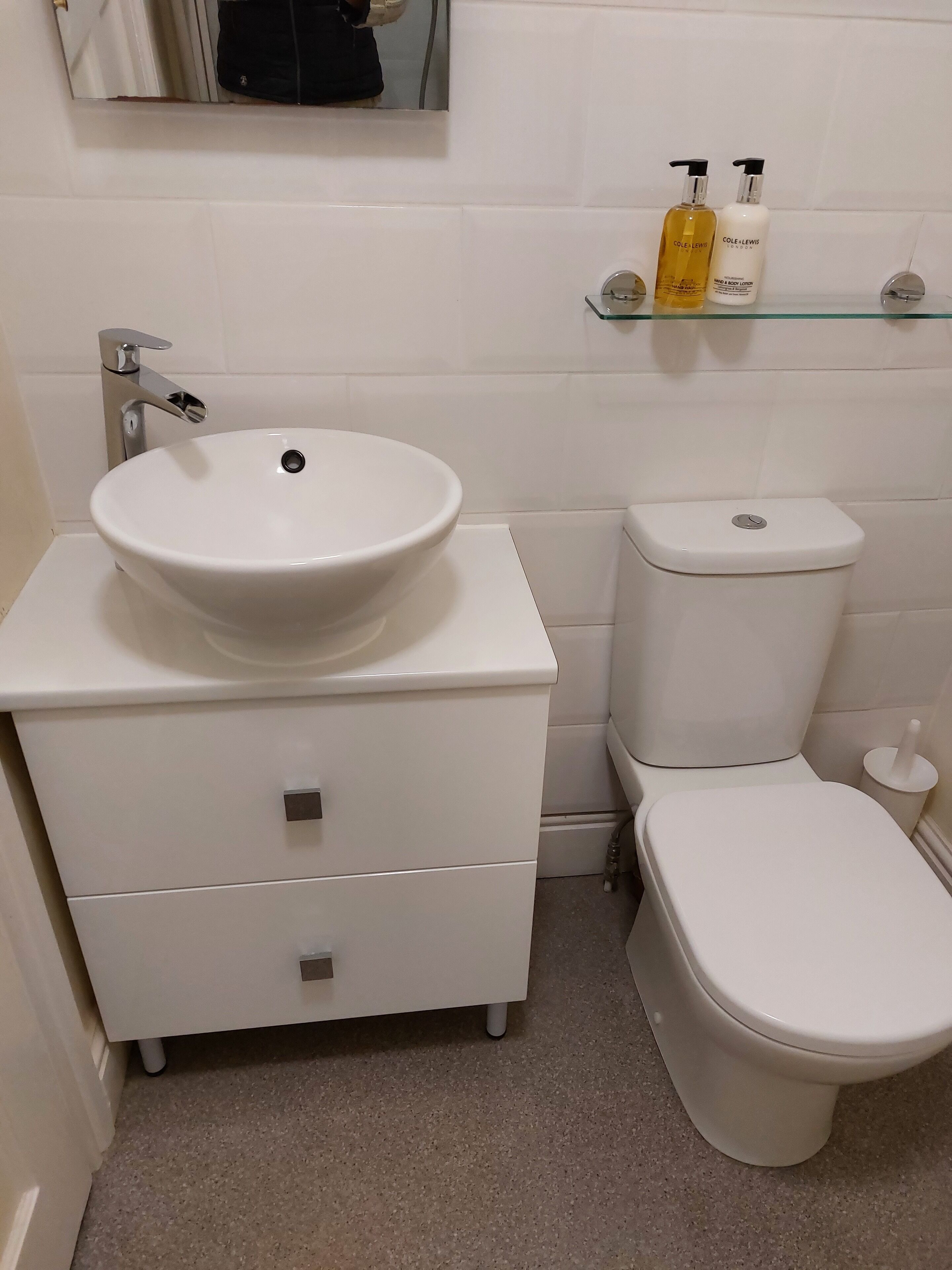 A bathroom with a white sink, toilet, and a small shelf with toiletries.