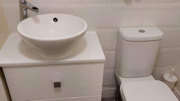 A bathroom with a white sink, toilet, and a small shelf with toiletries.