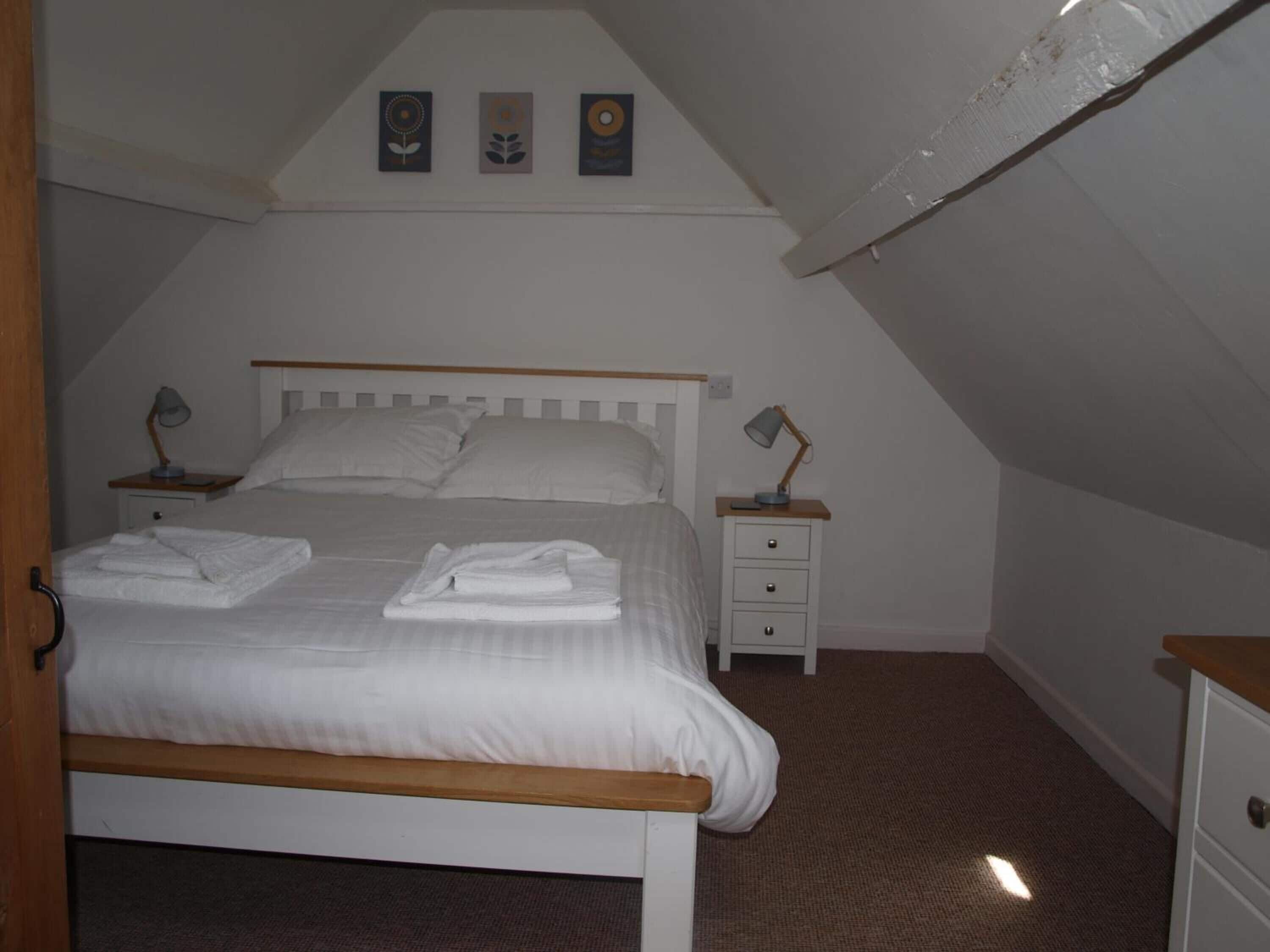 Un dormitorio con una cama, dos mesitas de noche y un mueble de noche, además de un techo con tres cuadros enmarcados.