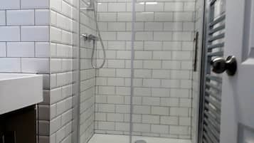 Un bany amb rajoles blanques tipus metro, un armari de dutxa de vidre, un vàter i un lavabo amb aixeta d'acer inoxidable.