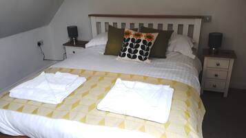 Cama bem arrumada com edredom estampado em padrão geométrico, duas almofadas com desenho floral e duas mesas de cabeceira com alto-falantes.