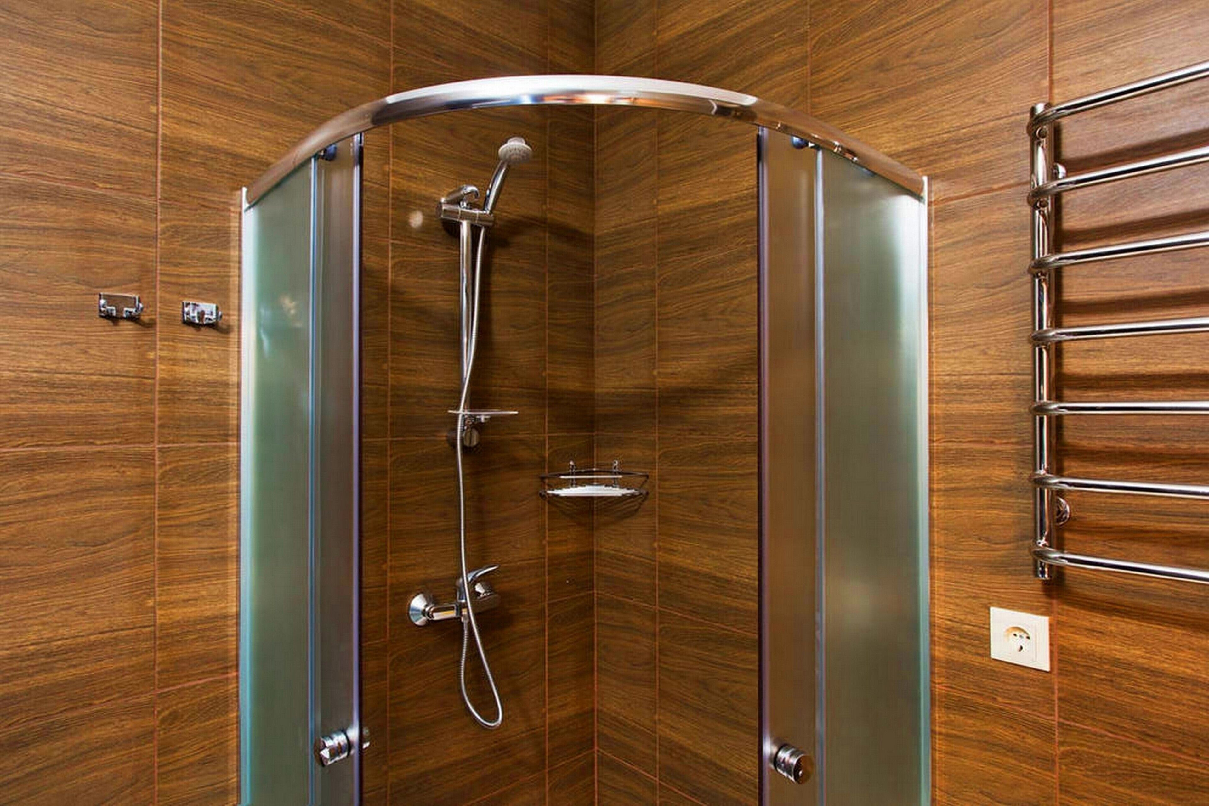 A corner shower with a glass enclosure, chrome fixtures, and a wooden wall.