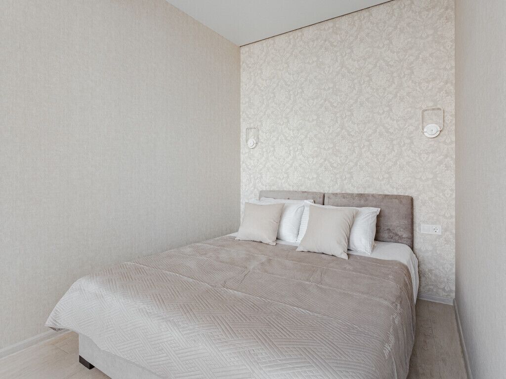 Un dormitorio con cama, cabecera y dos interruptores de luz en la pared.