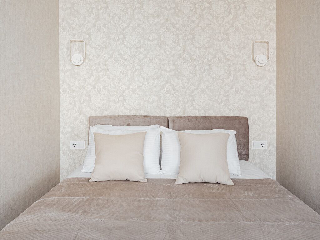 A bedroom with a bed, two pillows, a headboard, and two wall-mounted light fixtures.