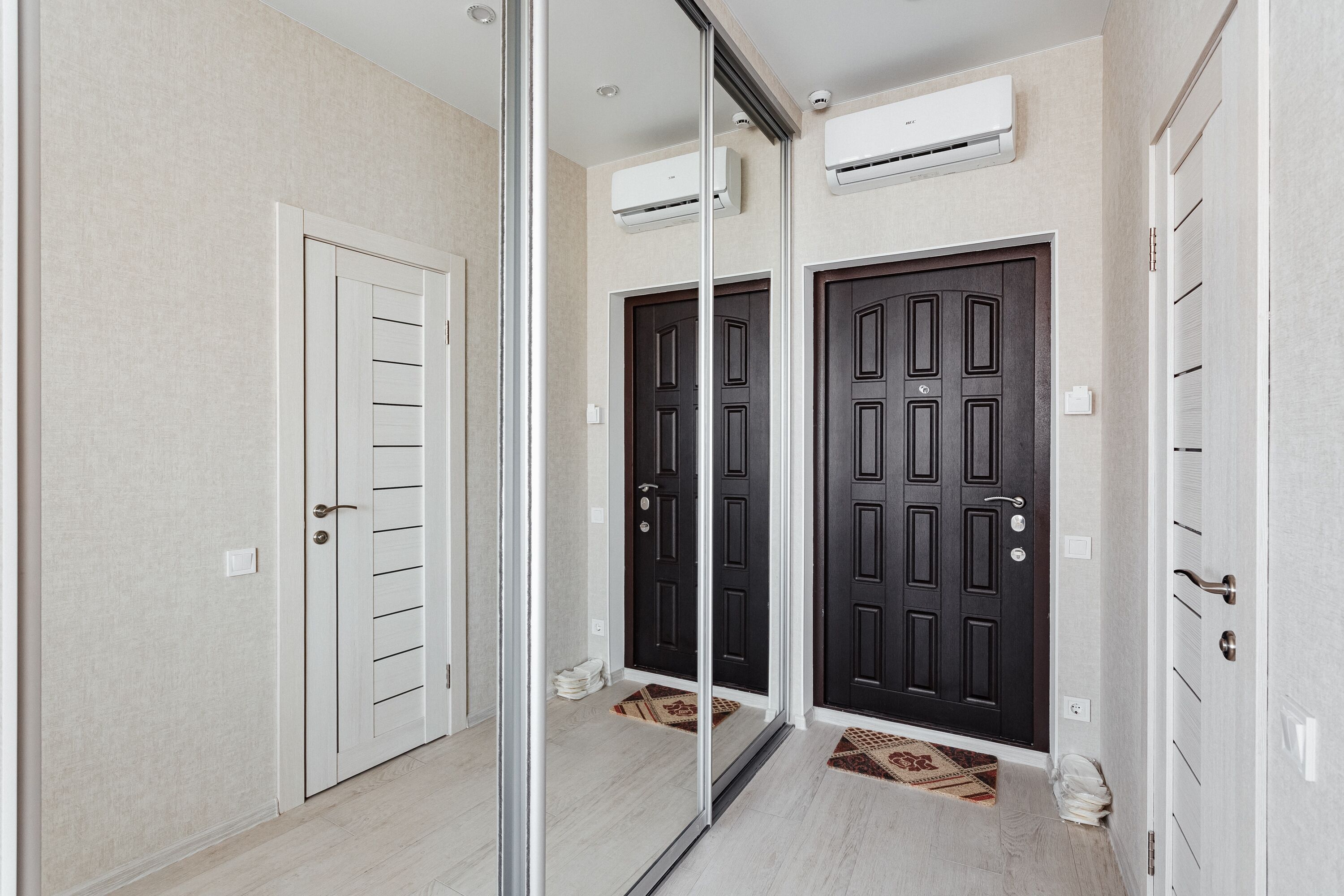 Un couloir avec une porte en verre, deux portes noires et une porte blanche. Des unités de climatisation sont fixées aux murs.