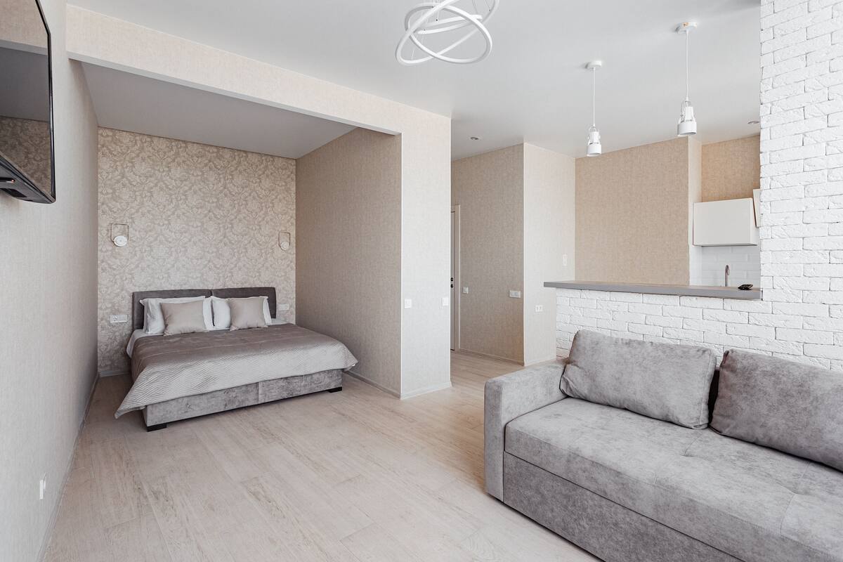 A modern bedroom with a bed, a grey sofa, and a white brick wall.