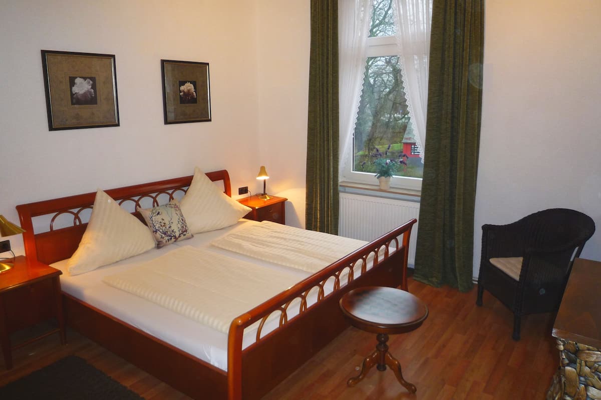 Une chambre à coucher avec un lit en bois, une table de chevet avec une lampe, une chaise et une fenêtre avec des rideaux.