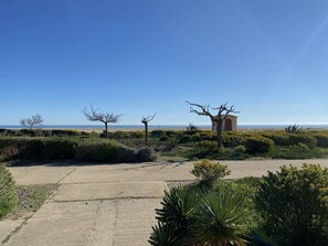 A paved pathway leading to a beach with sparse vegetation and a small building with a red door. - Beachfront Villa, 2 Rooms, 4 Guests - Port Leucate (Port Leucate)