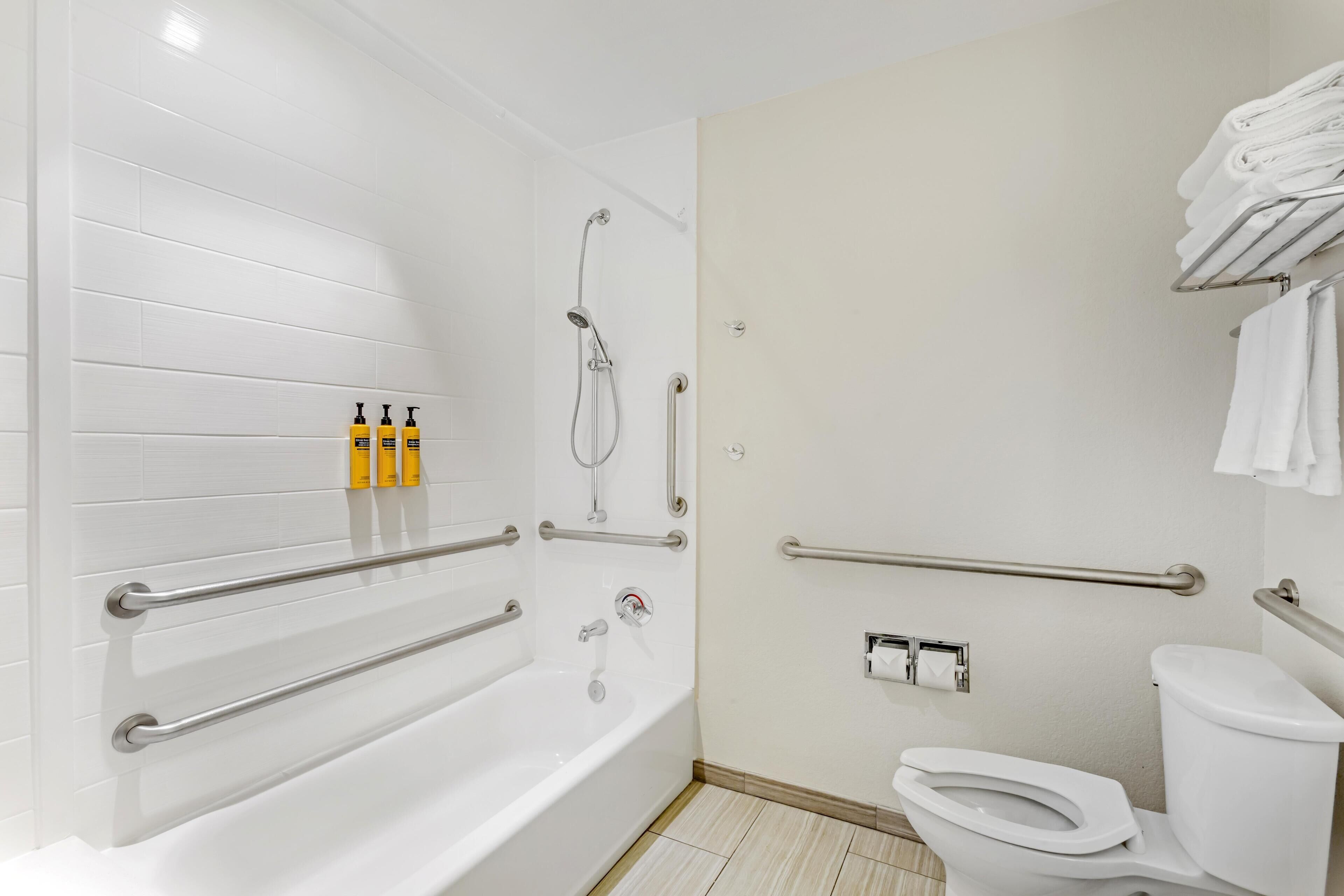 A bathroom with a bathtub, toilet, and handrails.