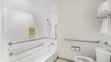 A bathroom with a bathtub, toilet, and handrails.
