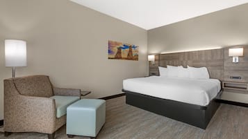 A hotel room with a bed, a chair, a nightstand, a lamp, and a painting on the wall.
