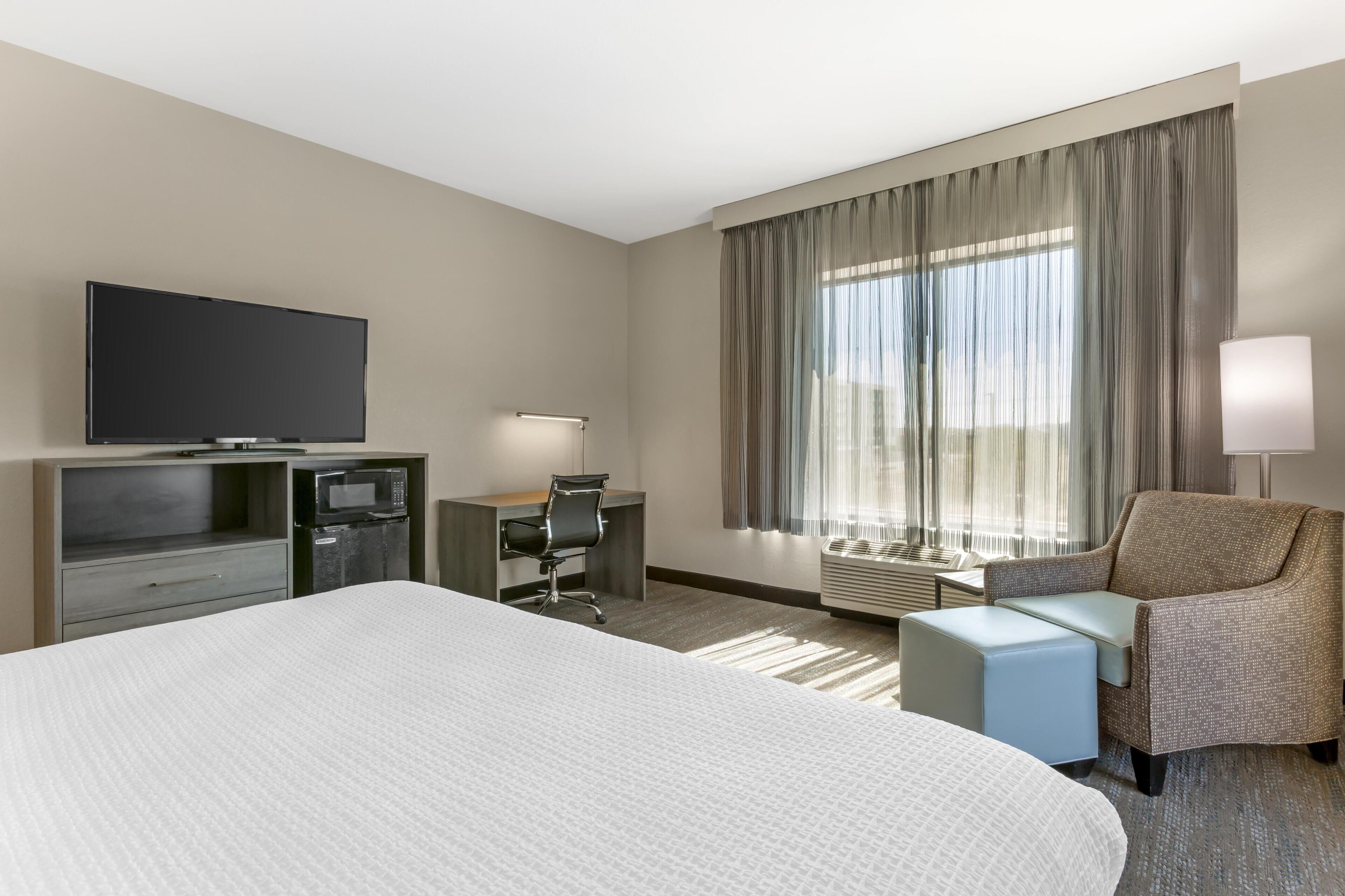 Una habitación de hotel con una cama grande, un escritorio con silla, televisión y ventana con cortinas.