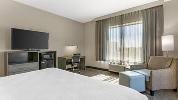 Una habitación de hotel con una cama grande, un escritorio con silla, televisión y ventana con cortinas.