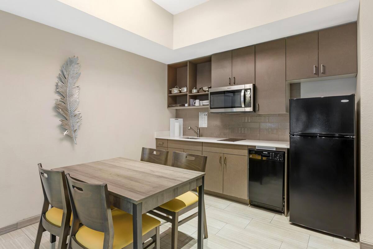 A compact kitchen with a dining table, chairs, a microwave, a refrigerator, and cabinets.