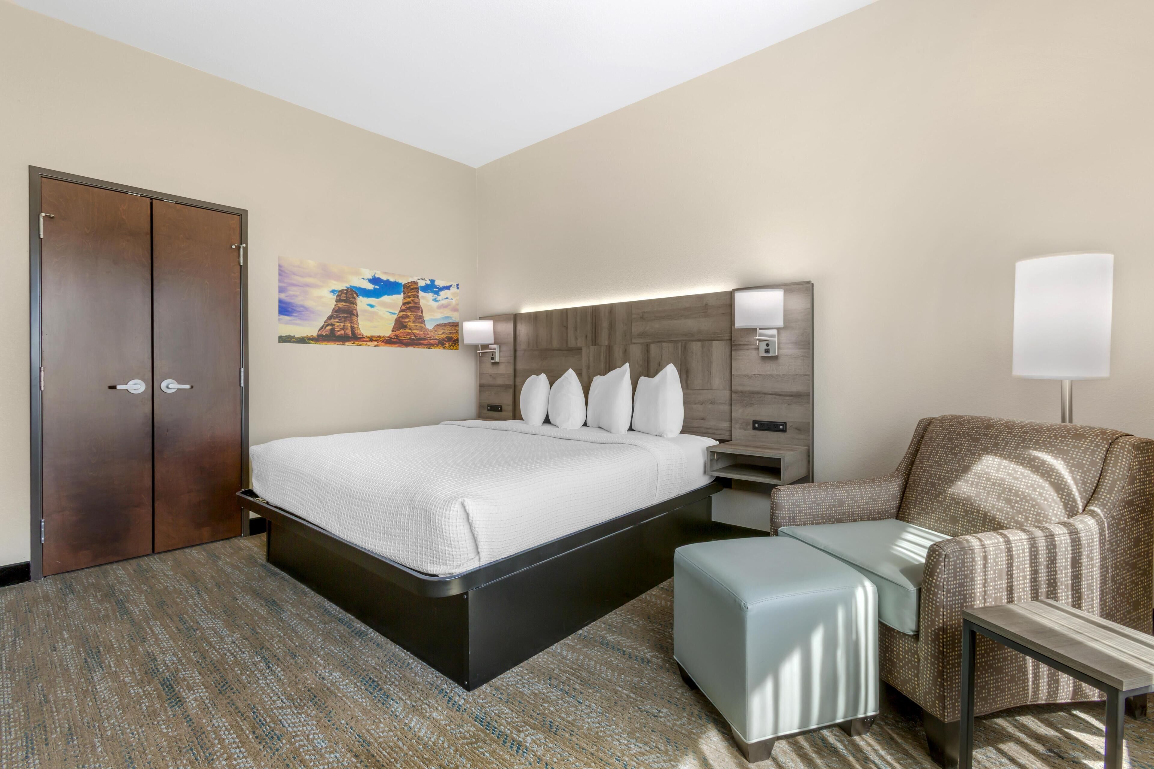 A hotel room with a bed, a chair, a desk, and a painting on the wall.