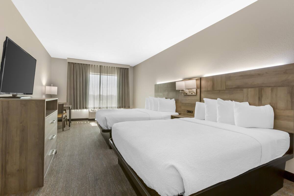 A hotel room with two beds, a TV, a desk, and a window with curtains.
