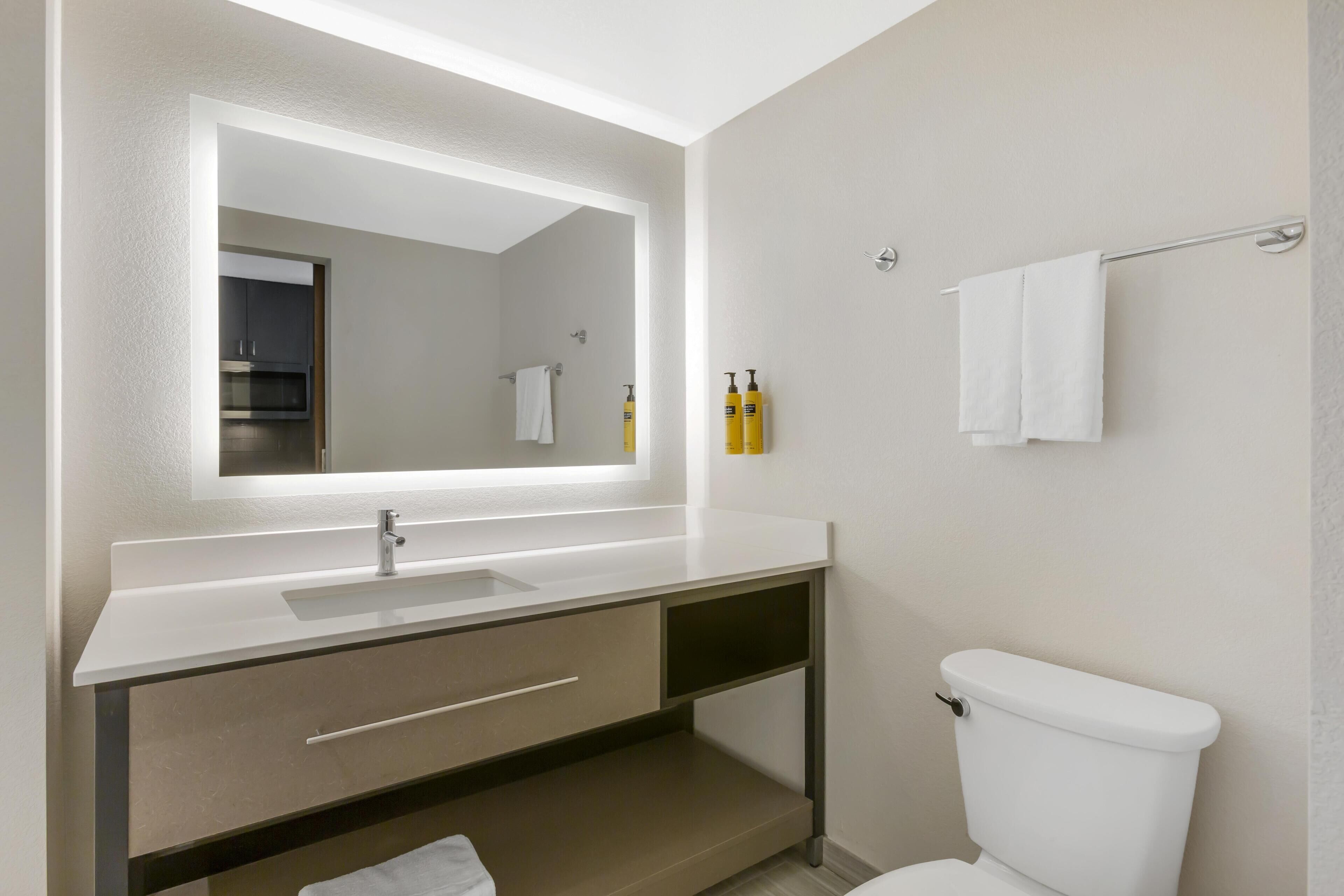 A modern bathroom with a white sink, a mirror, a toilet, and a towel rack.