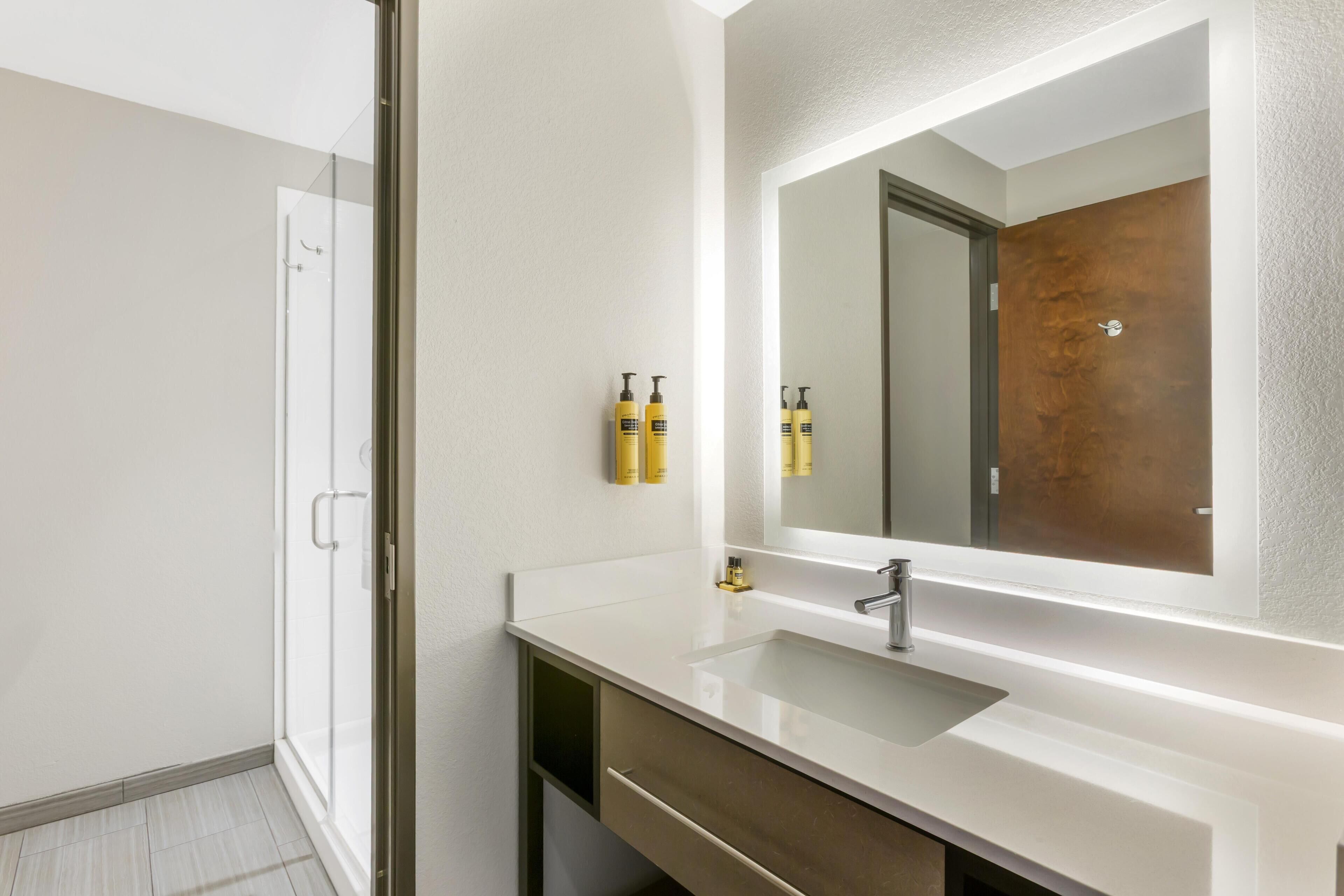 A modern bathroom with a white sink, a large mirror, and a glass shower enclosure.