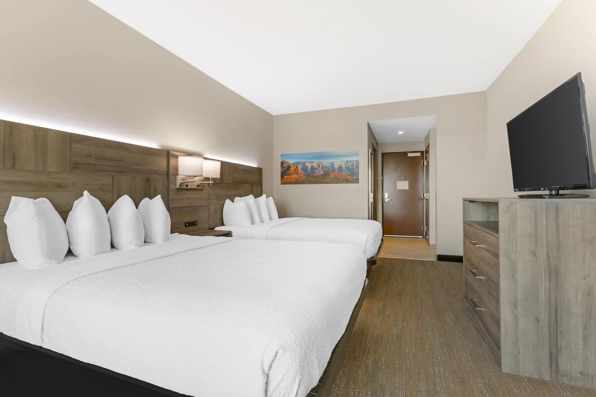 A hotel room with two beds, a flat-screen TV, a wooden headboard, a painting on the wall, and a wooden dresser.