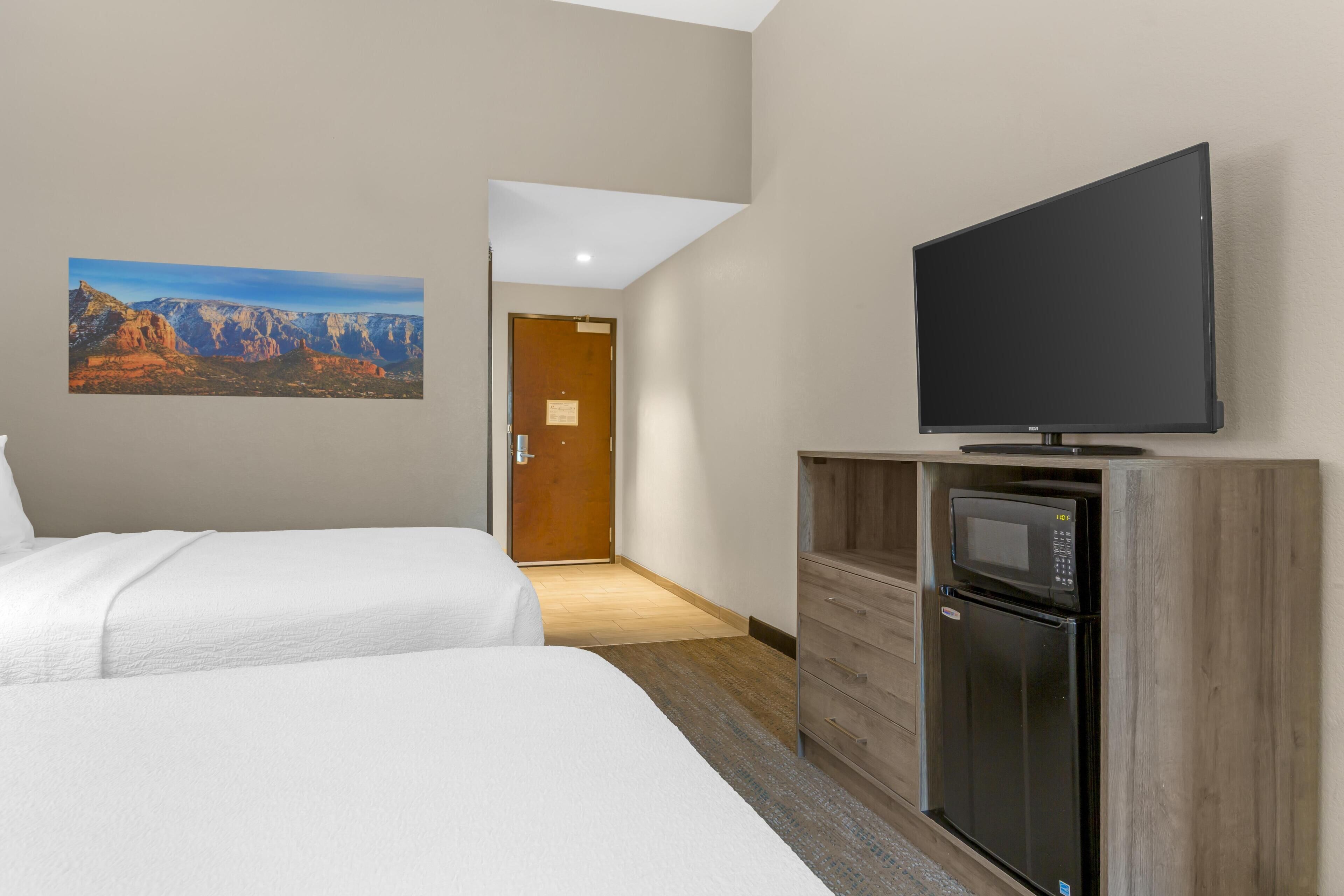 A hotel room with two beds, a flat-screen TV, a microwave, and a refrigerator.
