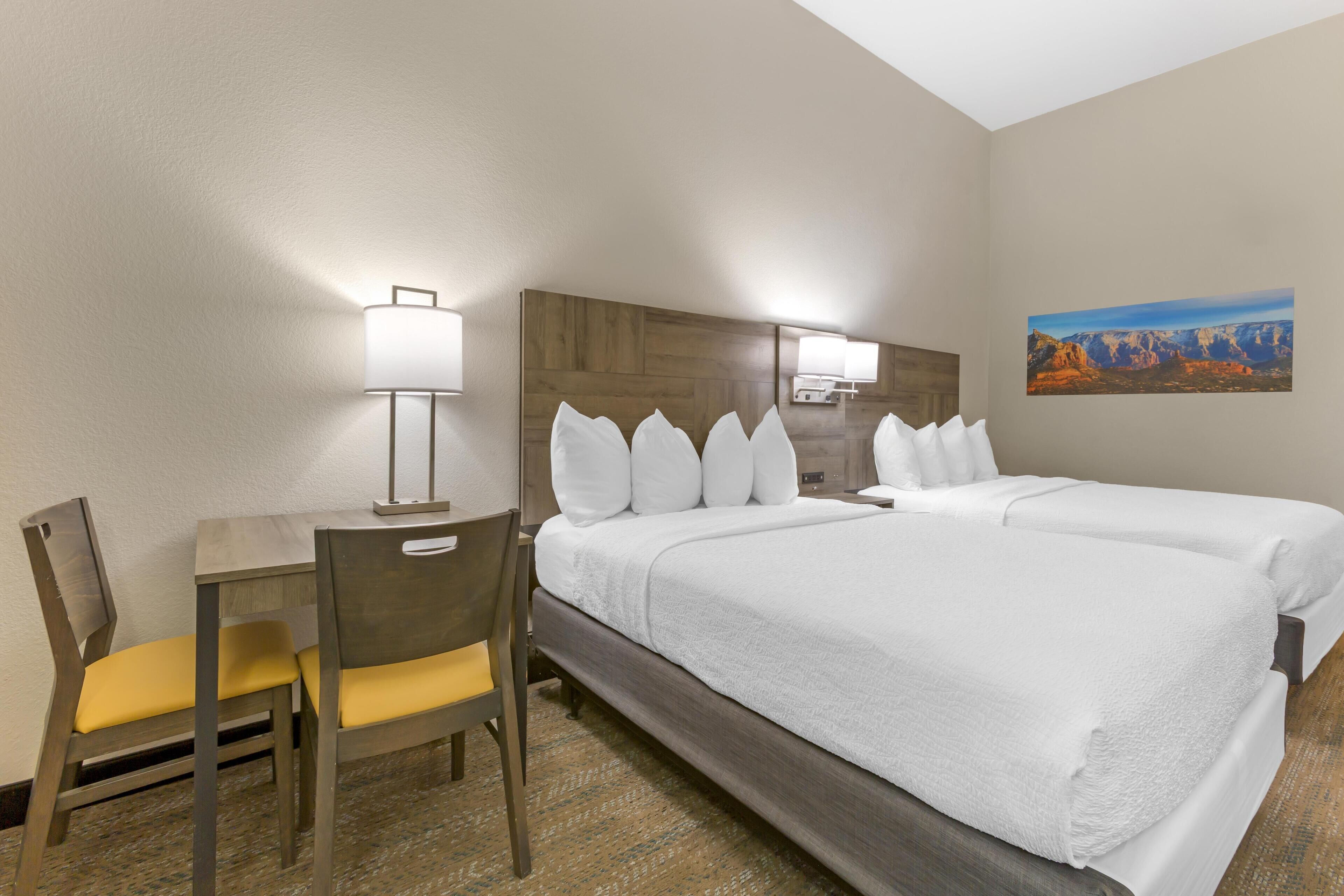A hotel room with a bed, a desk, a chair, and a lamp.