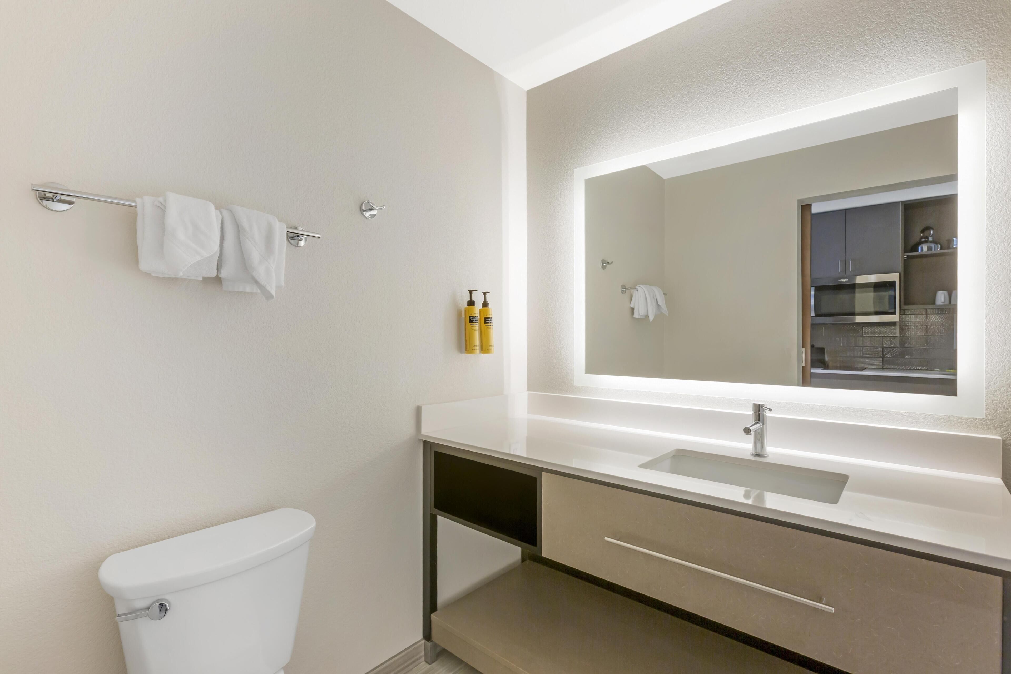 Un baño moderno con inodoro, lavamanos, espejo y toallero.