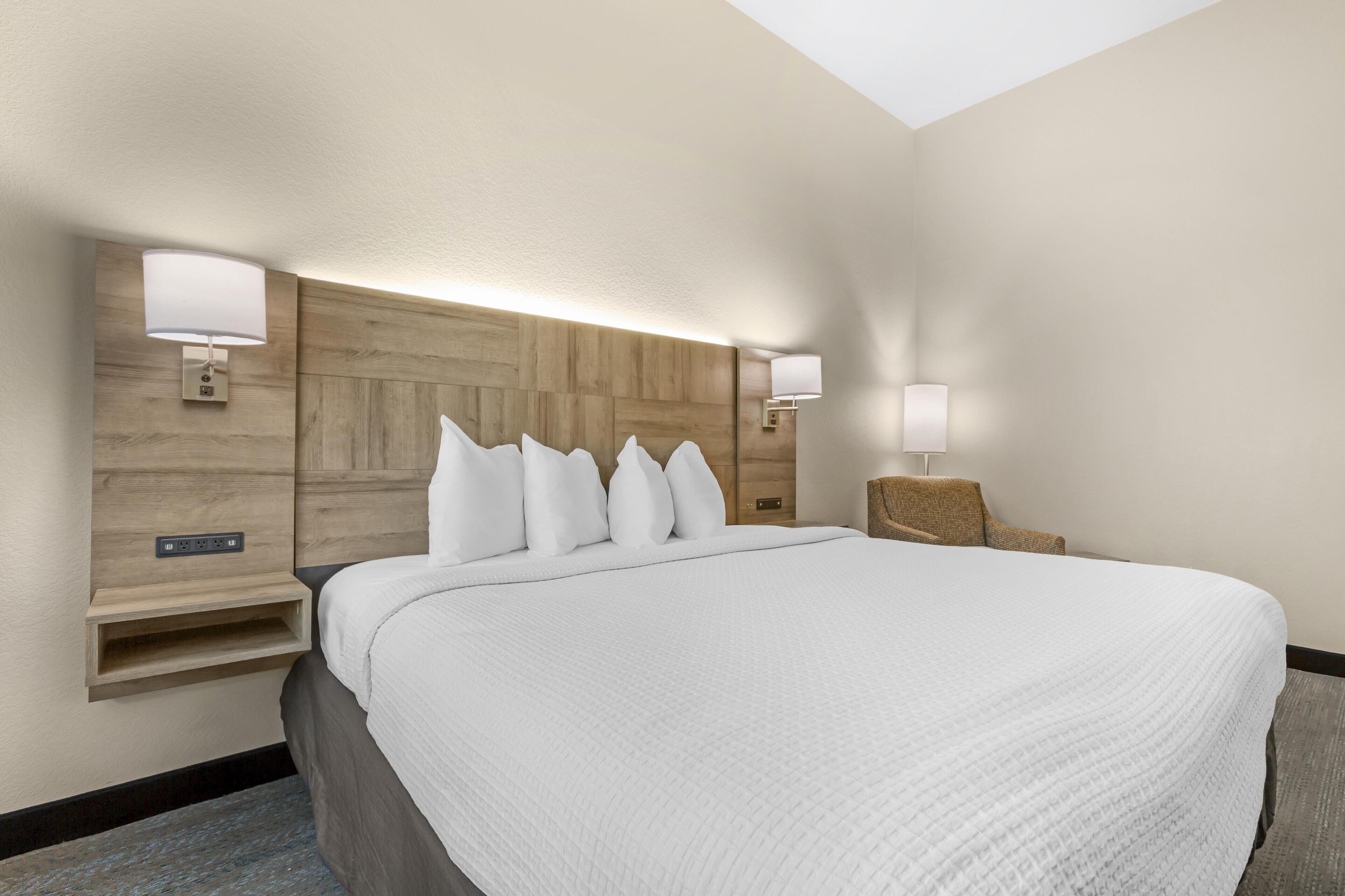 Une chambre d’hôtel avec un grand lit, deux tables de chevet, une tête de lit en bois et des lampes fixées au mur.