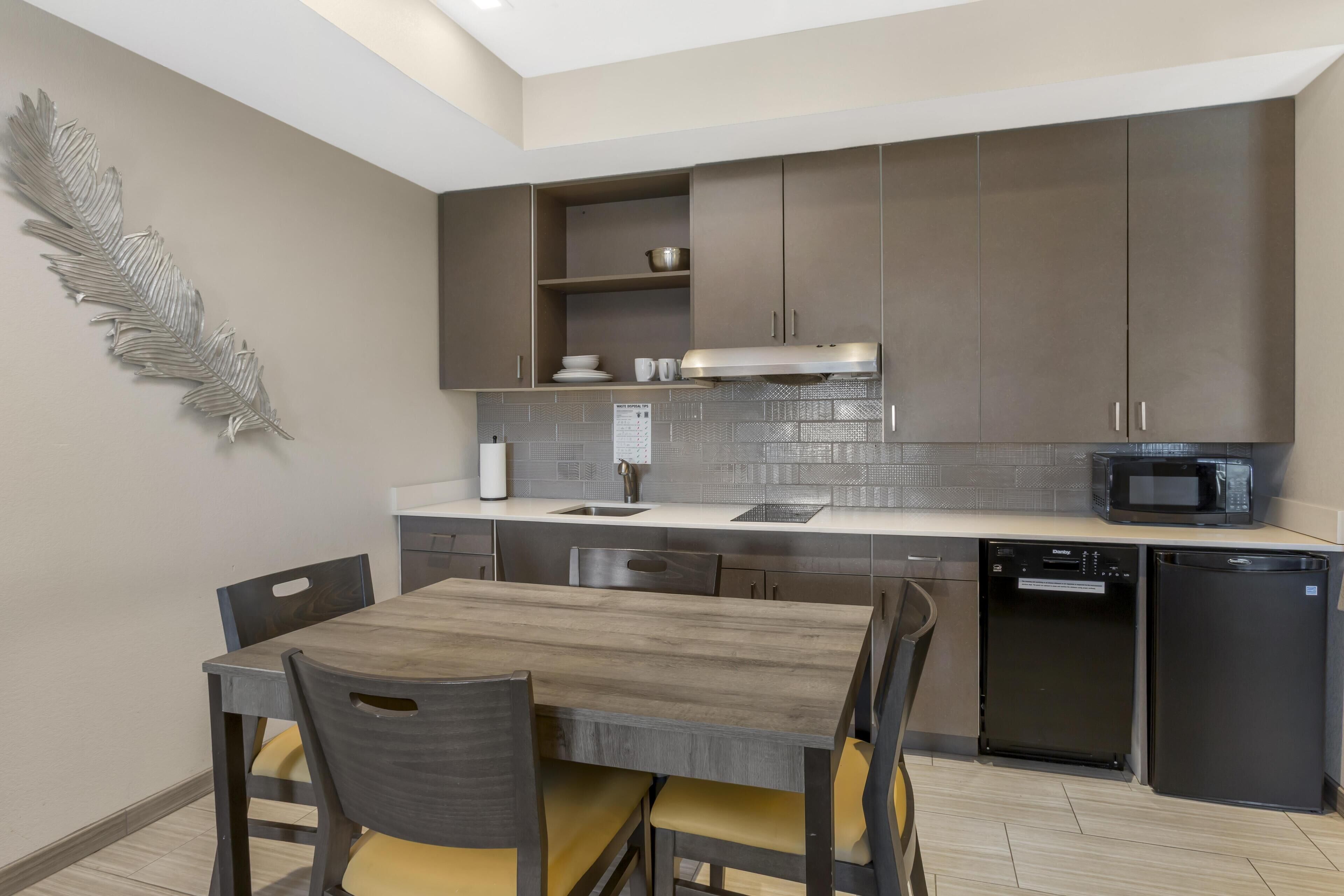 A modern kitchen with dark cabinets, a white countertop, a sink, a stove, a microwave, and a dishwasher.