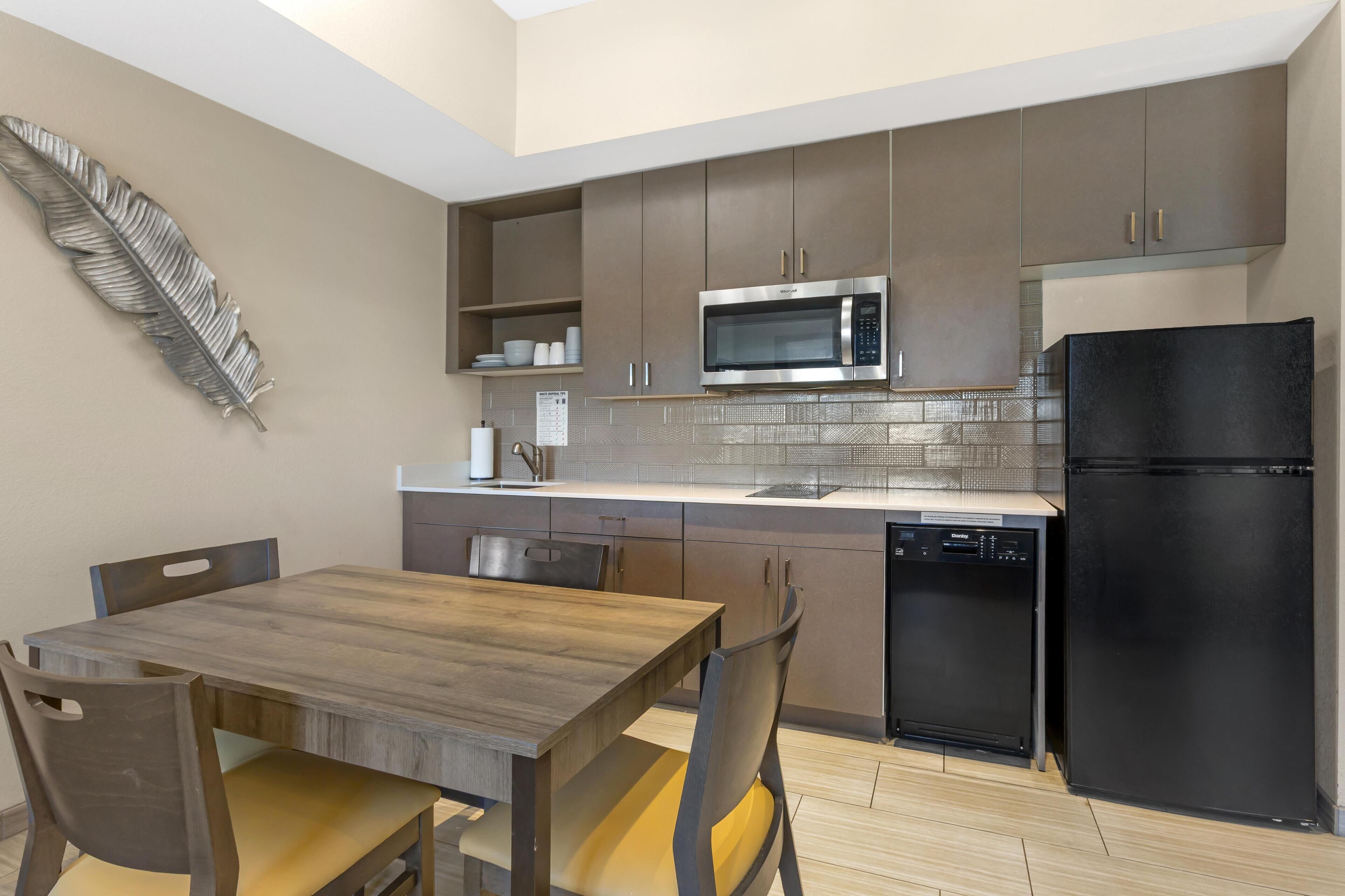 A modern kitchen with a wooden dining table, chairs, a microwave, a refrigerator, and a dishwasher.