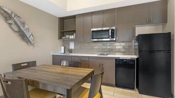 A modern kitchen with a wooden dining table, chairs, a microwave, a refrigerator, and a dishwasher.