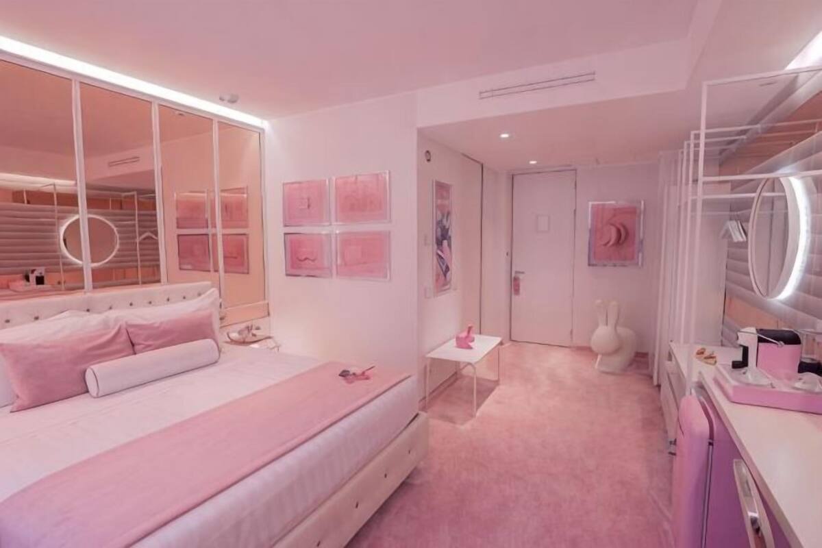 A pink-themed bedroom with a bed, bedside table, vanity, and a door.