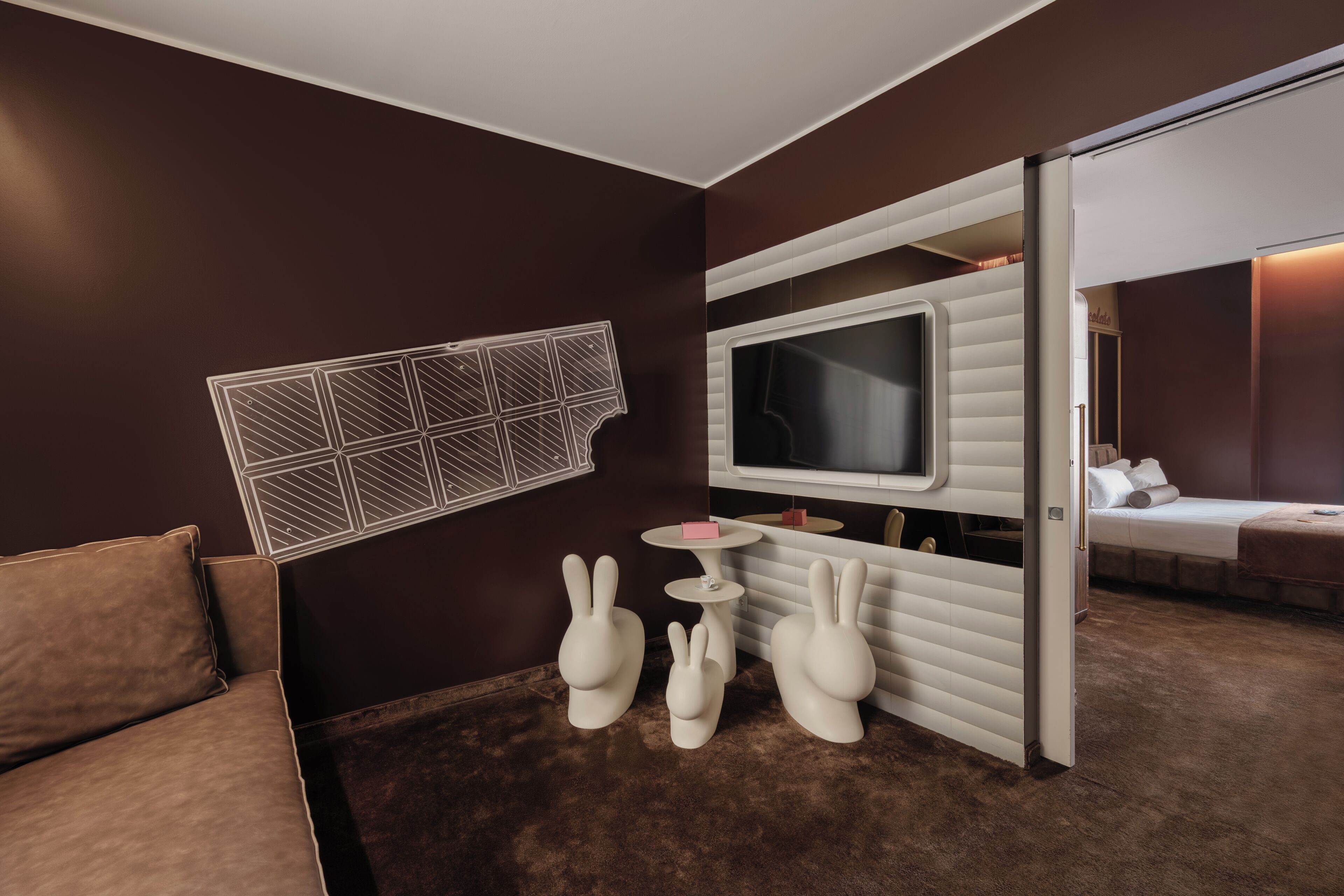 A room with a brown wall, a white sofa, a TV, and a small table with a pink object.