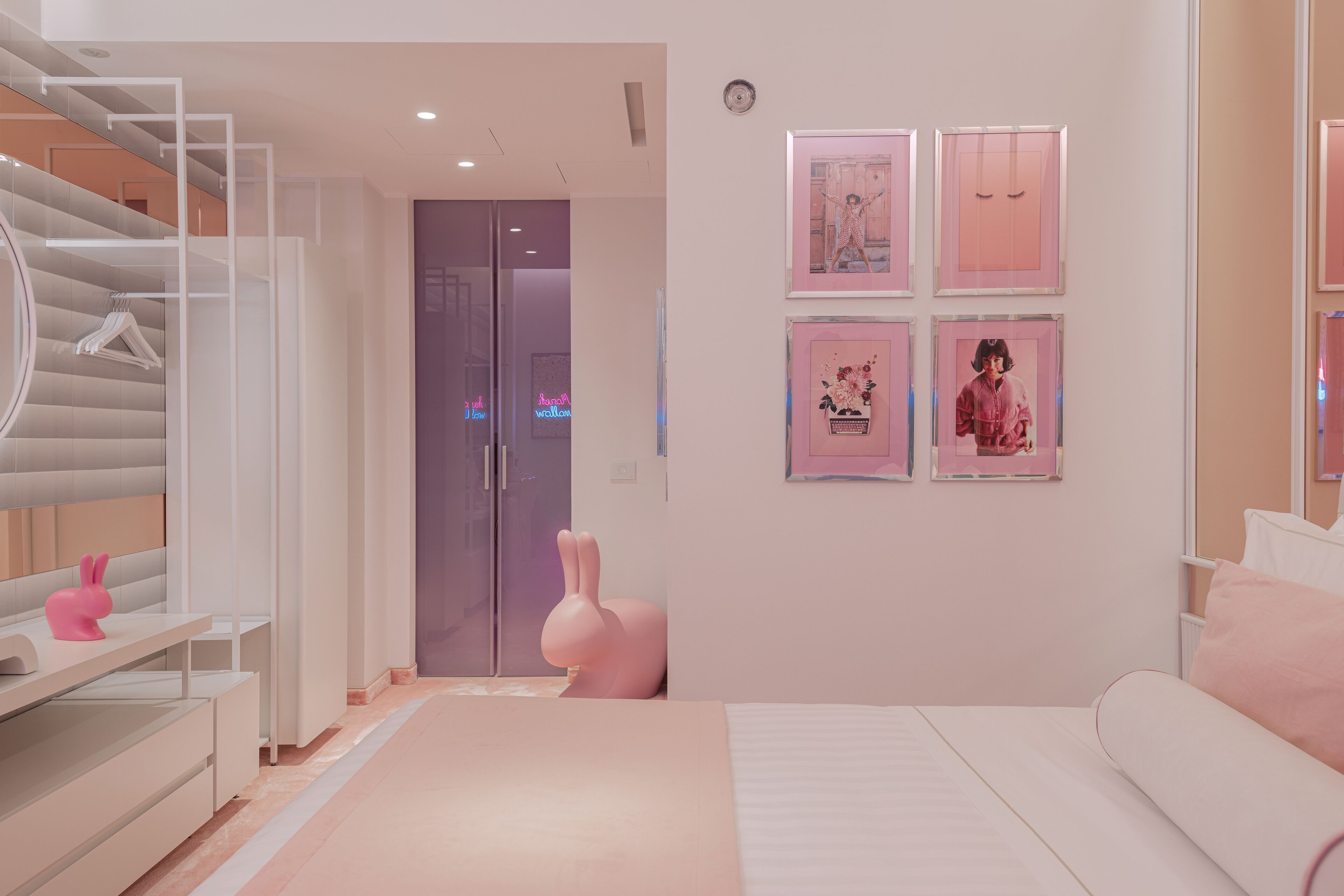A modern bedroom with a white bed, a pink bunny decoration, and framed artwork on the wall.