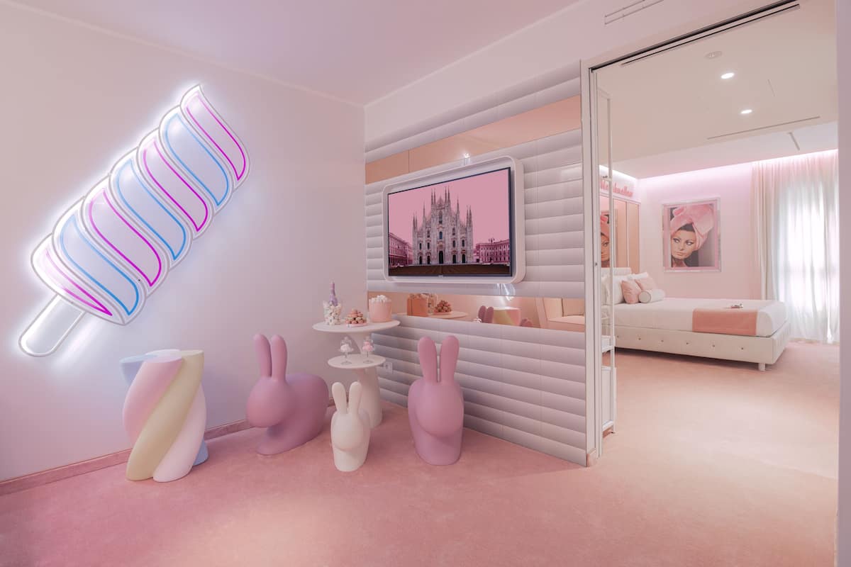 A modern, pink-themed room with a flat-screen TV, decorative bunny stools, and a unique wall-mounted light fixture.