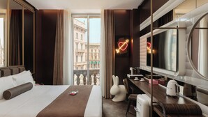 Quarto de hotel com cama, escrivaninha, cadeira, televisão e vista para edifícios.